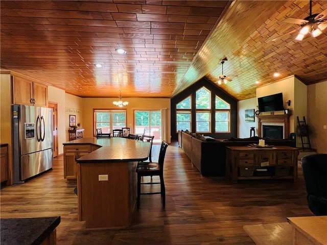 kitchen featuring stainless steel refrigerator with ice dispenser, dark wood-type flooring, a kitchen island, pendant lighting, and ceiling fan with notable chandelier