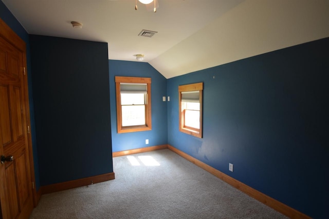 carpeted spare room featuring vaulted ceiling, baseboards, and visible vents