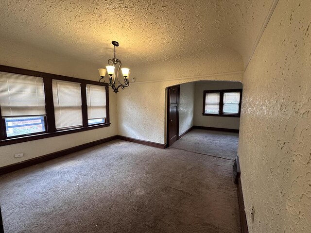 unfurnished room featuring a healthy amount of sunlight, a textured ceiling, a chandelier, and carpet floors