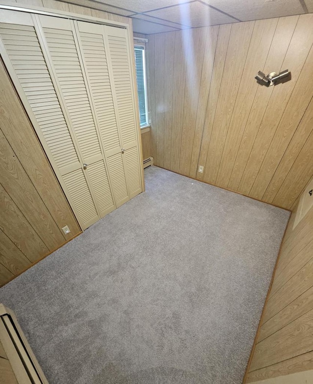 unfurnished bedroom featuring a baseboard heating unit, a closet, light colored carpet, and wooden walls