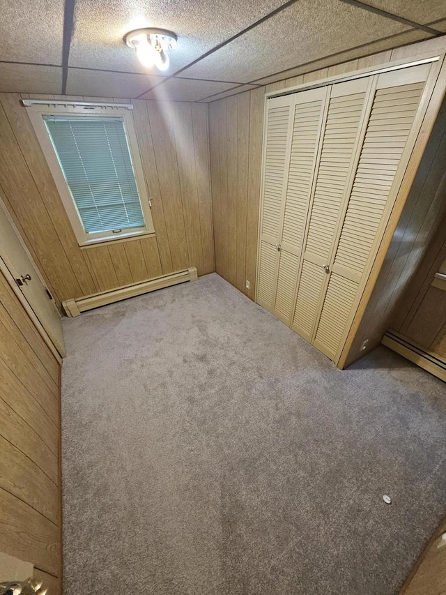 unfurnished bedroom featuring carpet floors, a baseboard radiator, a closet, and wooden walls