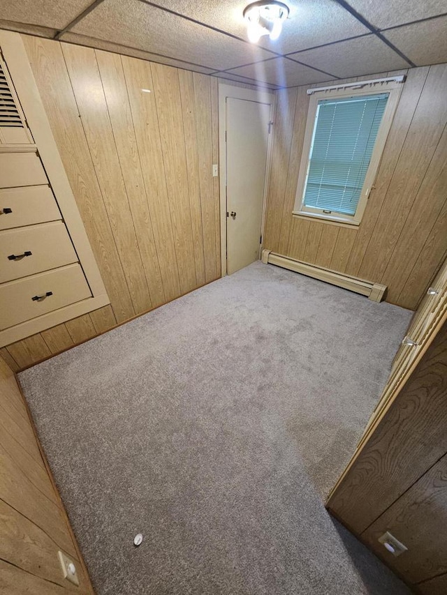 unfurnished bedroom featuring wooden walls, a paneled ceiling, carpet floors, and a baseboard radiator