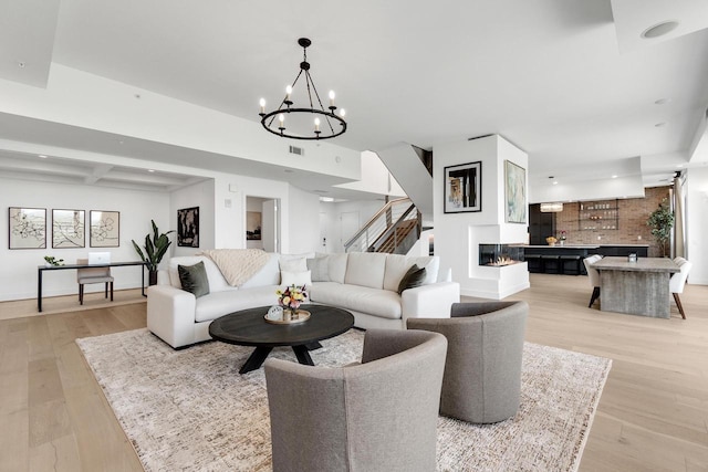 living room with beam ceiling, an inviting chandelier, and light hardwood / wood-style flooring