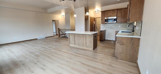 kitchen with tasteful backsplash, sink, hanging light fixtures, a center island, and light hardwood / wood-style floors