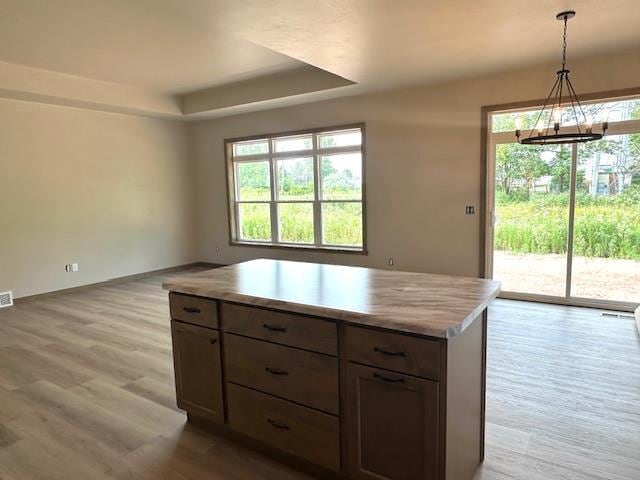 kitchen featuring hanging light fixtures, a wealth of natural light, light hardwood / wood-style floors, a kitchen island, and a raised ceiling