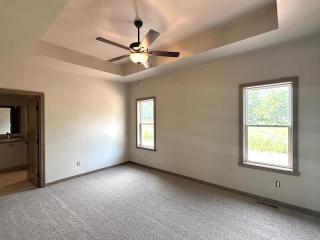 empty room with a raised ceiling, sink, light carpet, and ceiling fan