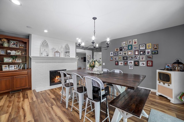 dining space featuring a fireplace, hardwood / wood-style floors, and an inviting chandelier