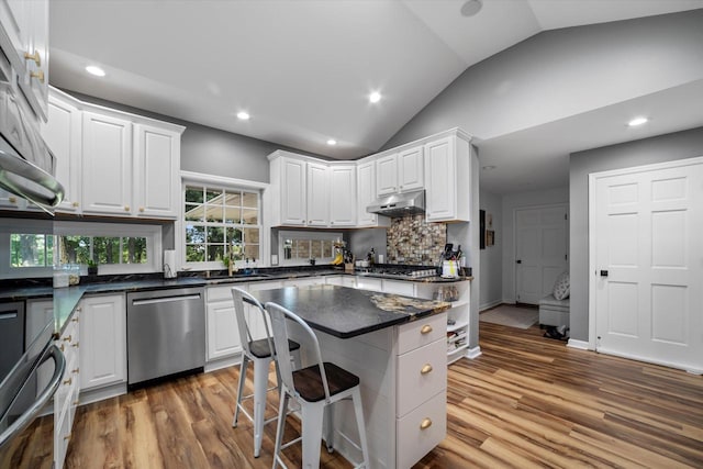 kitchen with lofted ceiling, a kitchen breakfast bar, stainless steel appliances, and hardwood / wood-style flooring