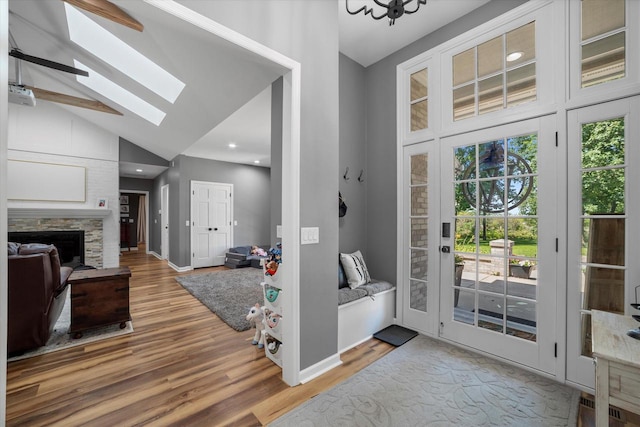 entrance foyer with wood-type flooring, a skylight, a stone fireplace, and high vaulted ceiling