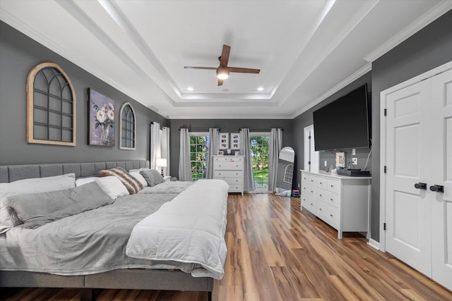 bedroom featuring wood-type flooring, crown molding, a raised ceiling, and ceiling fan