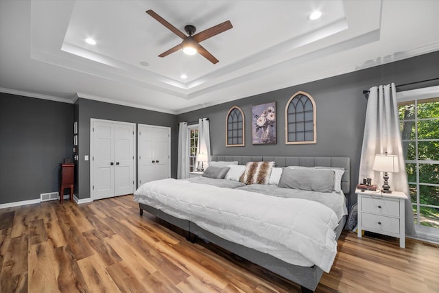 bedroom featuring ceiling fan, a raised ceiling, light wood-type flooring, and multiple closets