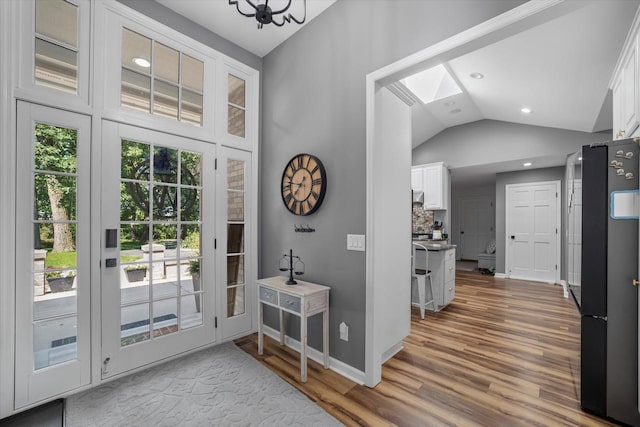 doorway featuring a skylight, high vaulted ceiling, and light hardwood / wood-style floors