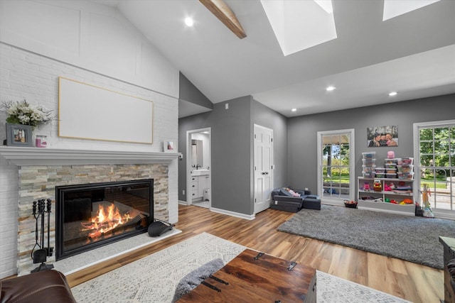 living room with a skylight, light hardwood / wood-style flooring, a stone fireplace, and beam ceiling