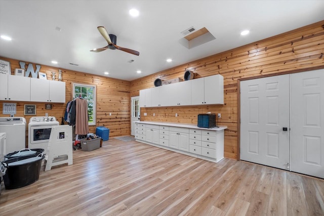 kitchen featuring wood walls, light hardwood / wood-style flooring, white cabinets, and washer and clothes dryer