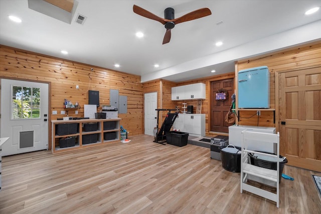 workout room with ceiling fan, wooden walls, light hardwood / wood-style floors, and electric panel