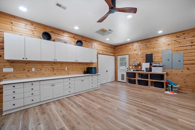 kitchen featuring light wood-type flooring, electric panel, ceiling fan, white cabinets, and wood walls