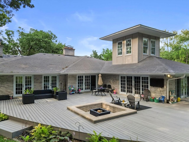 rear view of property featuring french doors, a wooden deck, and an outdoor living space with a fire pit