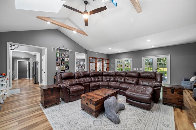 living room with a skylight, high vaulted ceiling, ceiling fan, french doors, and light hardwood / wood-style floors