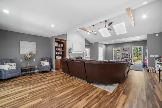 living room featuring a skylight, a stone fireplace, light wood-type flooring, ceiling fan, and beam ceiling