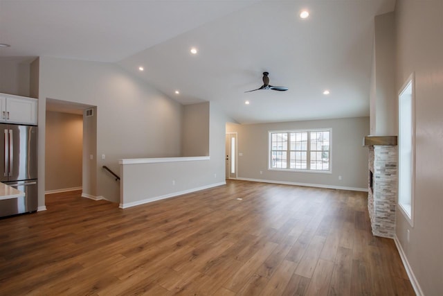 unfurnished living room with a fireplace, lofted ceiling, ceiling fan, wood finished floors, and baseboards