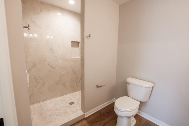 full bathroom with tiled shower, wood finished floors, toilet, and baseboards