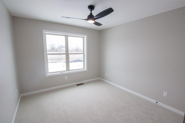 spare room with light colored carpet, ceiling fan, visible vents, and baseboards