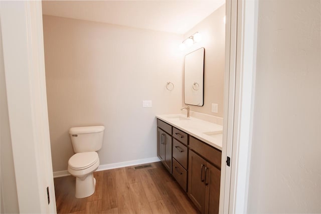 bathroom with double vanity, toilet, a sink, wood finished floors, and baseboards