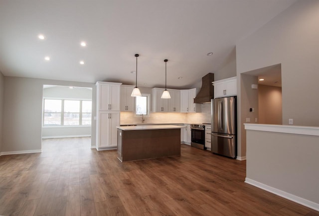 kitchen featuring light countertops, hanging light fixtures, appliances with stainless steel finishes, a kitchen island, and premium range hood