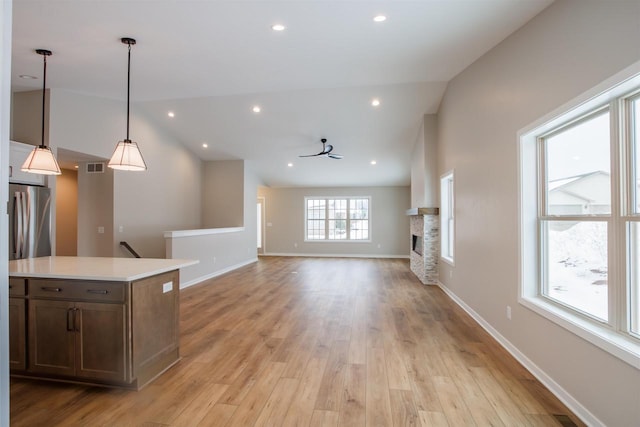 unfurnished living room with a fireplace, visible vents, light wood-style floors, vaulted ceiling, and baseboards