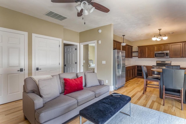 living room featuring ceiling fan with notable chandelier and light wood-type flooring