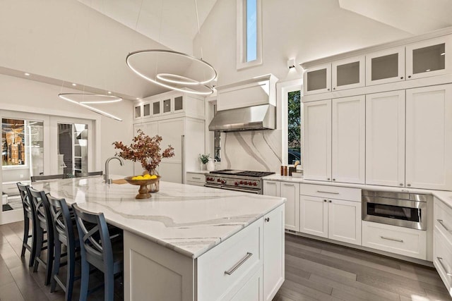 kitchen with exhaust hood, a center island with sink, pendant lighting, dark wood-type flooring, and stainless steel appliances