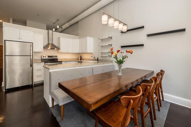 interior space featuring kitchen peninsula, appliances with stainless steel finishes, white cabinets, and wall chimney range hood