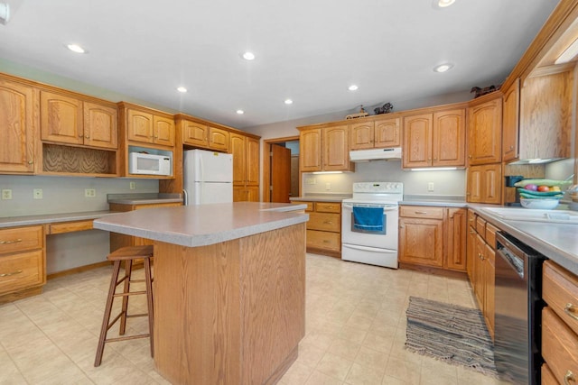 kitchen with a breakfast bar, sink, a center island, built in desk, and white appliances