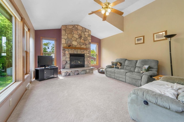 carpeted living room with ceiling fan, a stone fireplace, vaulted ceiling, and a wealth of natural light