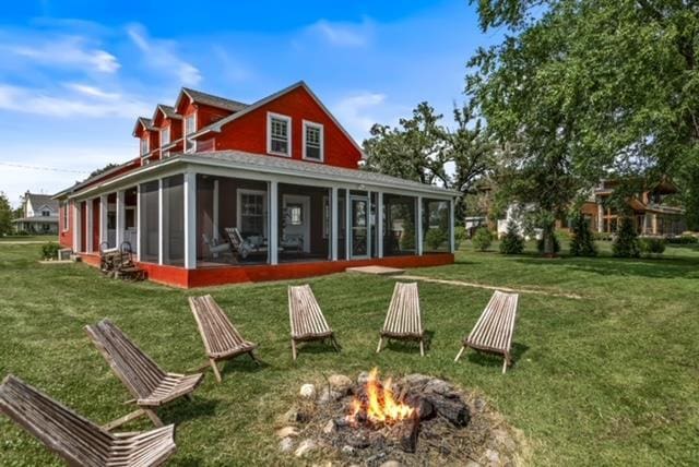 back of house featuring a sunroom, an outdoor fire pit, and a lawn