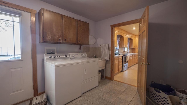 clothes washing area with washer and clothes dryer, light tile patterned floors, plenty of natural light, and cabinets