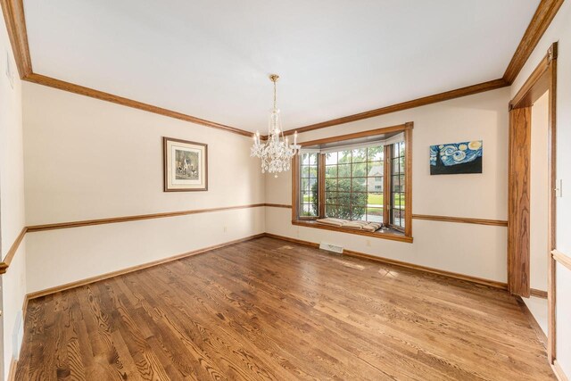 empty room featuring crown molding, wood-type flooring, and an inviting chandelier