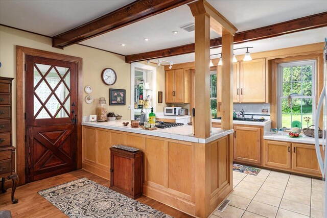 kitchen featuring kitchen peninsula, tasteful backsplash, light tile patterned flooring, and beam ceiling