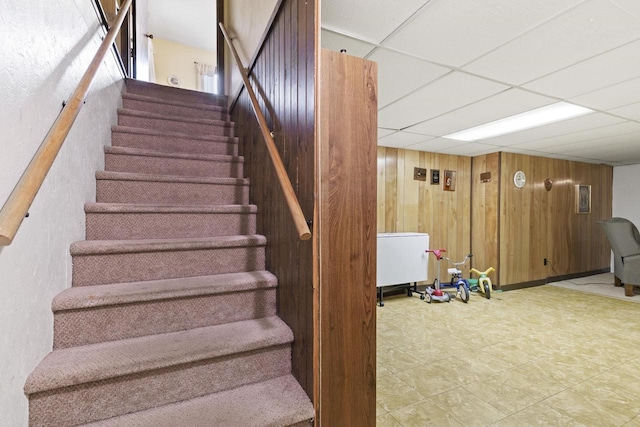 stairway featuring wooden walls and a drop ceiling