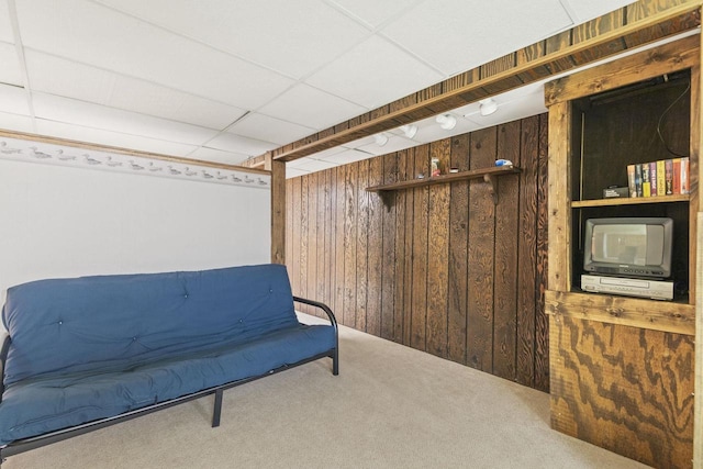 living area featuring carpet, a paneled ceiling, and wood walls