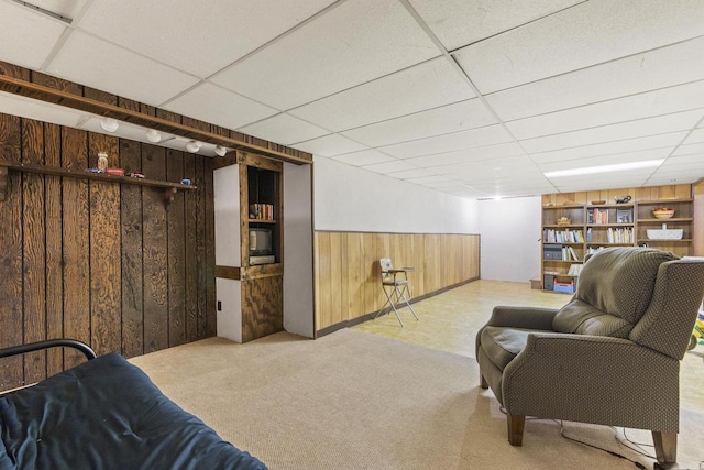 carpeted living room featuring wooden walls, a drop ceiling, and built in shelves