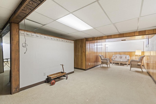 sitting room featuring light carpet, a drop ceiling, and wood walls