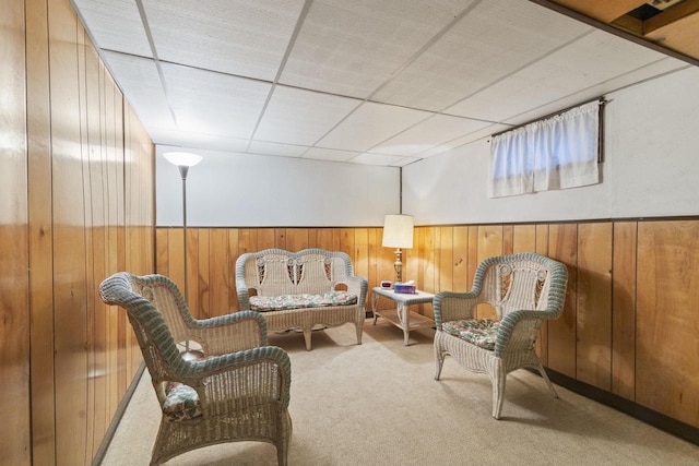 living area featuring a drop ceiling, carpet flooring, and wood walls