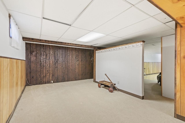 basement with a paneled ceiling, carpet, and wood walls