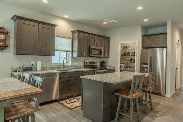 kitchen featuring light wood-type flooring, light stone countertops, stainless steel appliances, and dark brown cabinetry