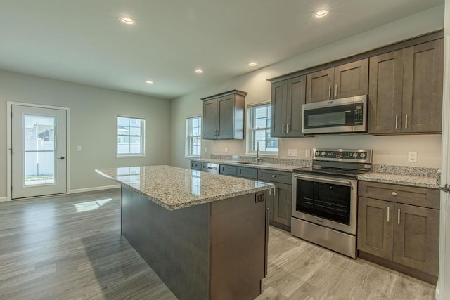 kitchen with sink, a center island, light hardwood / wood-style floors, stainless steel appliances, and light stone countertops