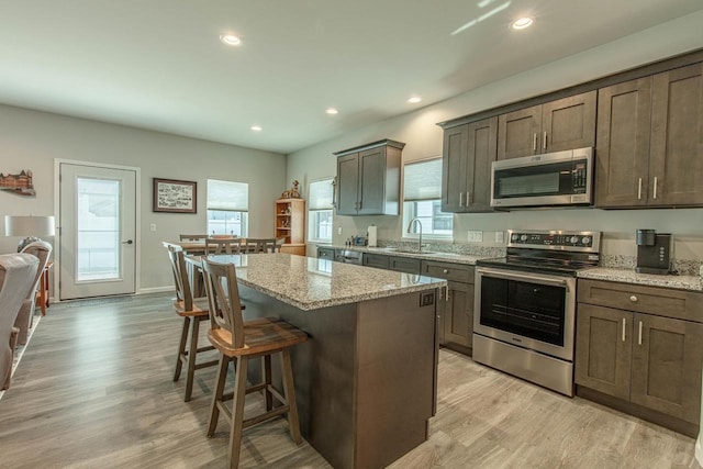 kitchen featuring a wealth of natural light, appliances with stainless steel finishes, a kitchen island, and light stone counters