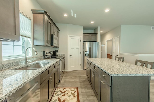 kitchen with a breakfast bar area, stainless steel appliances, light stone counters, a kitchen island, and sink