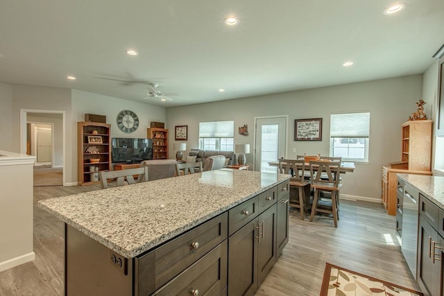 kitchen with a healthy amount of sunlight, light stone countertops, a kitchen island, and light hardwood / wood-style floors