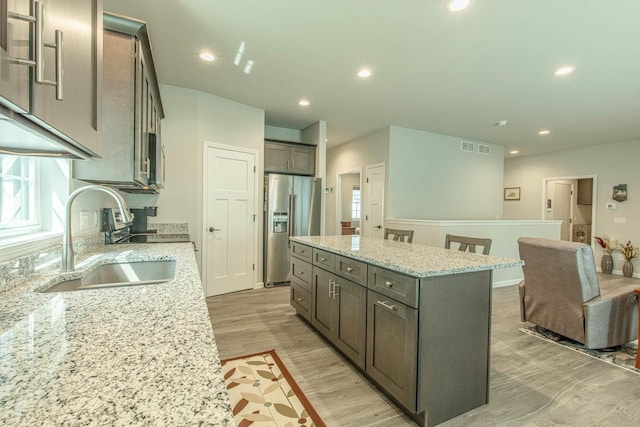 kitchen featuring light wood-type flooring, high end refrigerator, a kitchen island, sink, and light stone counters